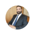 A professional man with a beard is sitting in an office, dressed in a suit and tie.